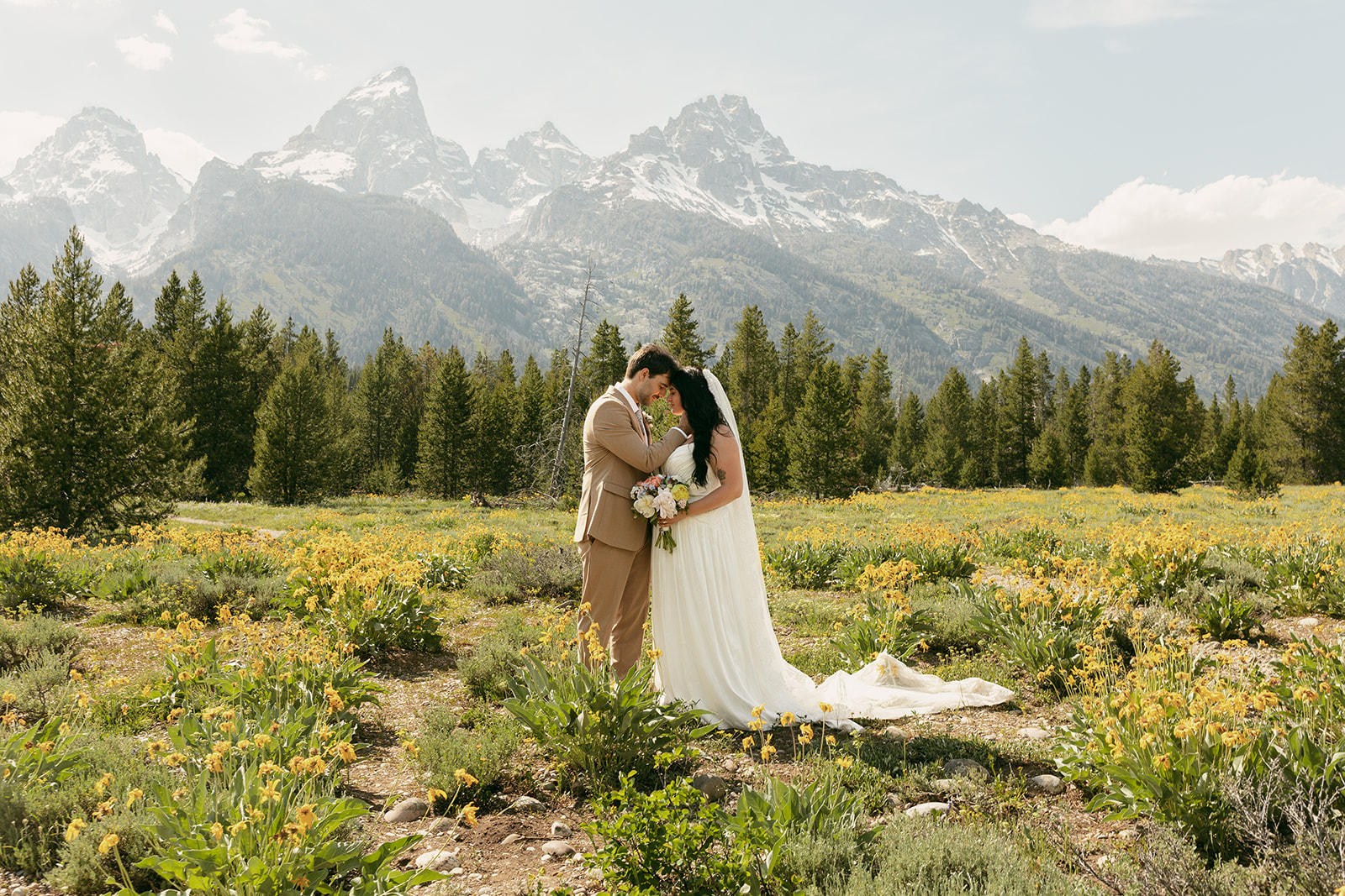 Bride and groom embrace in a wildflower field beneath the Teton peaks during their intimate wedding in the Grand Tetons.