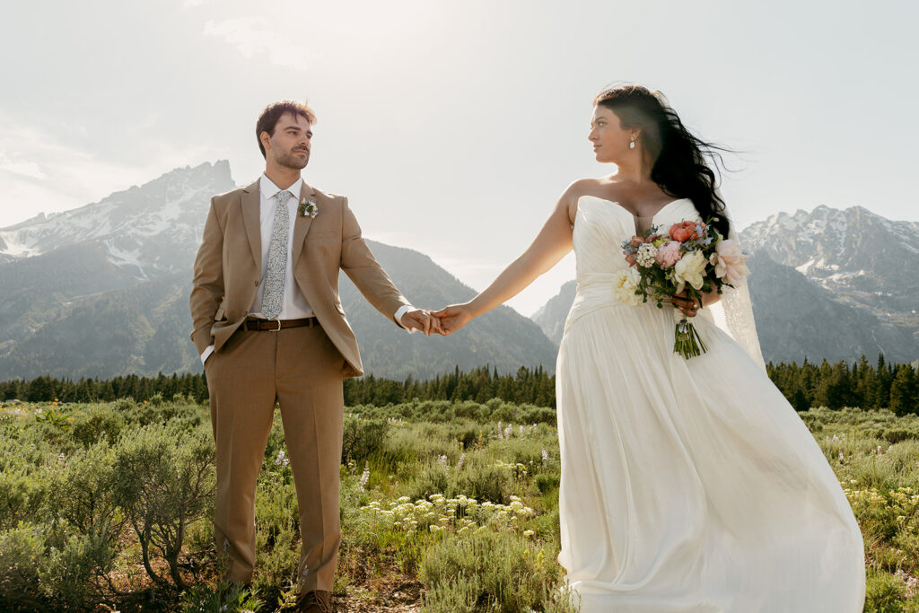 Intimate wedding in the Grand Tetons with the couple holding hands in front of sunlit mountain peaks.