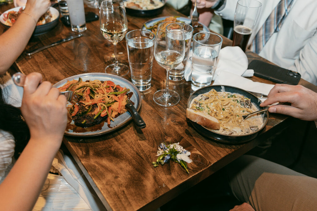 Close-up of plated wedding reception meals with pasta, grilled vegetables, and wine glasses.