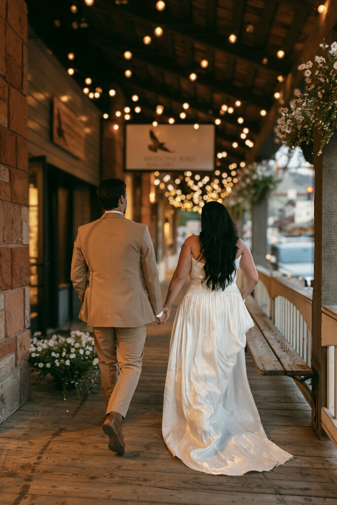 Bride and groom walk hand in hand beneath glowing string lights in downtown Jackson Hole after intimate wedding in the Grand Tetons