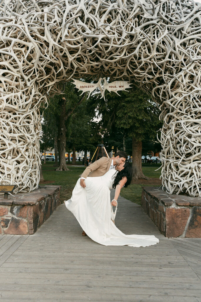 Groom dips bride in front of iconic antler arch in Jackson Hole, Wyoming, after their elopement.