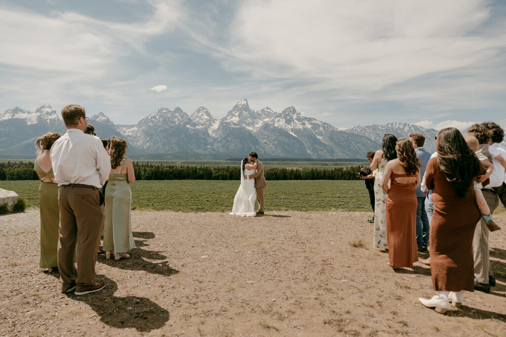 Couple shares a kiss after their ceremony with family gathered and the Grand Tetons as a backdrop.