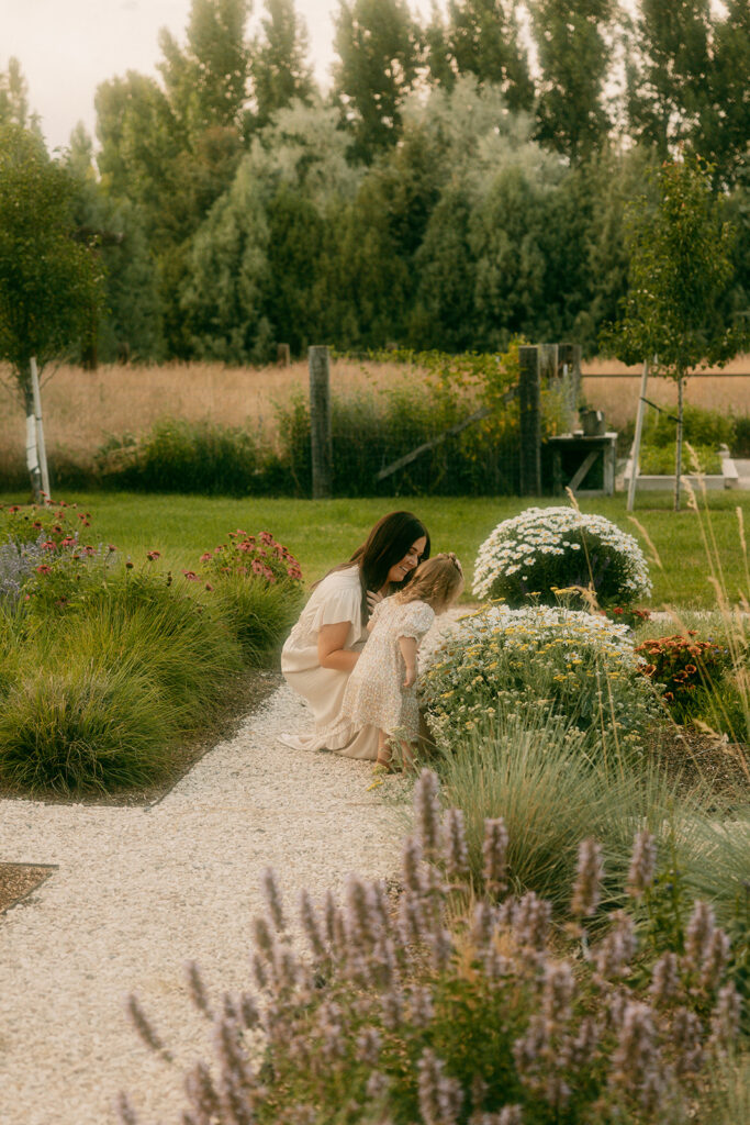 Mother and daughter kneel beside daisies in a garden path at sunset in Idaho Falls.