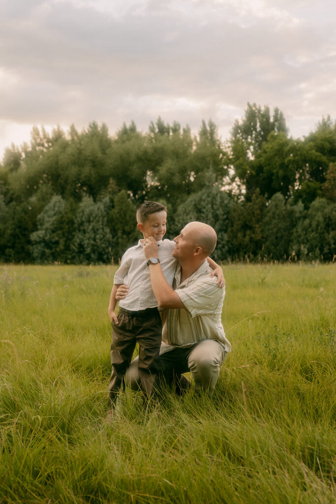 Father and son share a tender moment kneeling in the grass at an Idaho Falls family session.