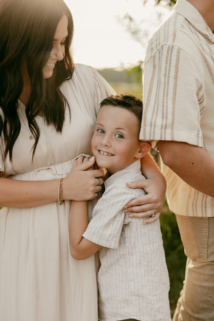 Mother wrapping arms around her smiling son during a warm sunset family photo.