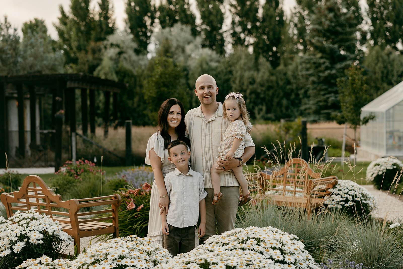 Family of four standing close together in a flower garden, smiling during golden hour.