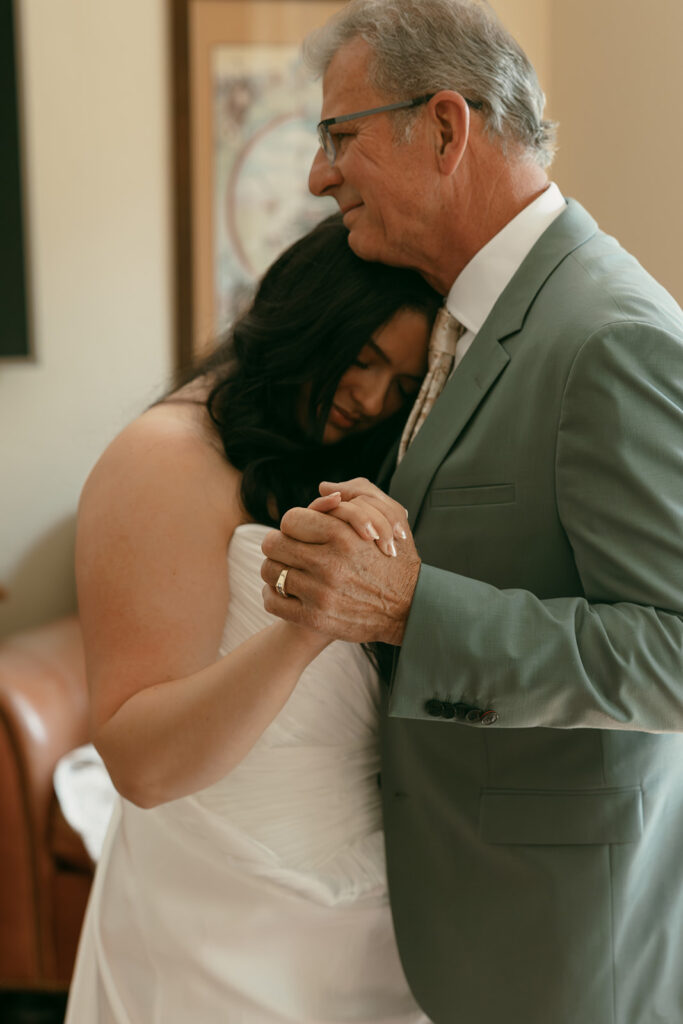 Bride rests her head on father’s shoulder during a quiet, emotional moment before the ceremony.