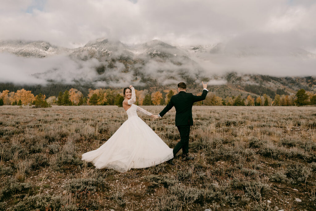 Bride and groom celebrate while holding hands in front of the Grand Tetons.