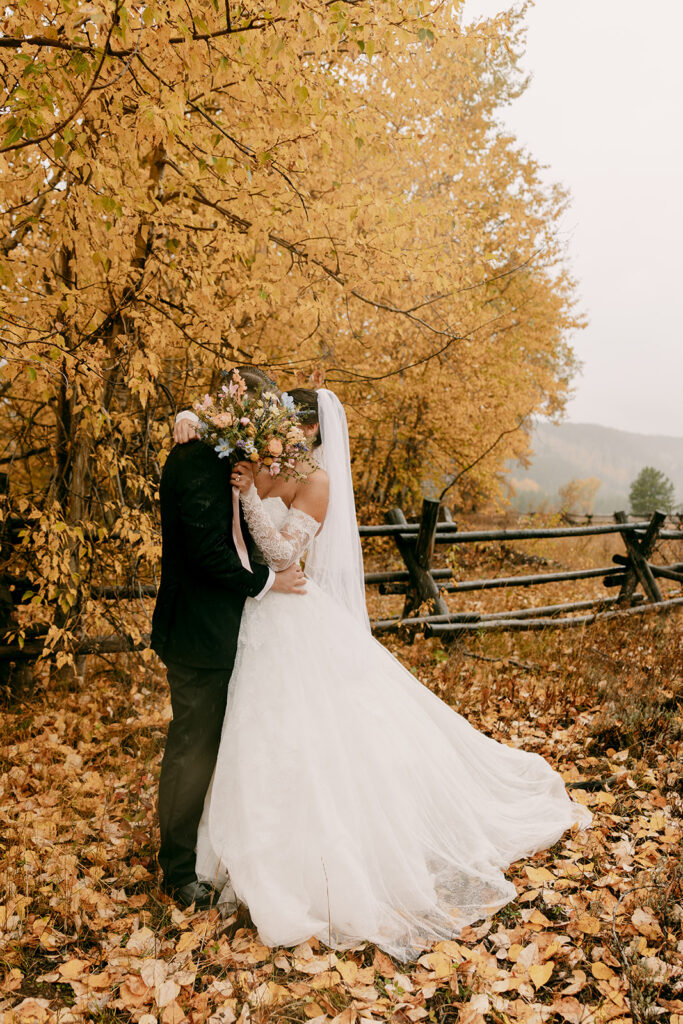 Bride and groom share a kiss hidden behind bridal bouquet.