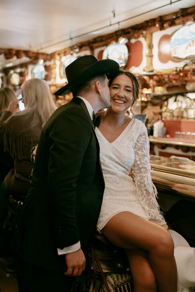 Groom kisses bride's cheek inside the Million Dollar Cowboy bar in Jackson Hole.